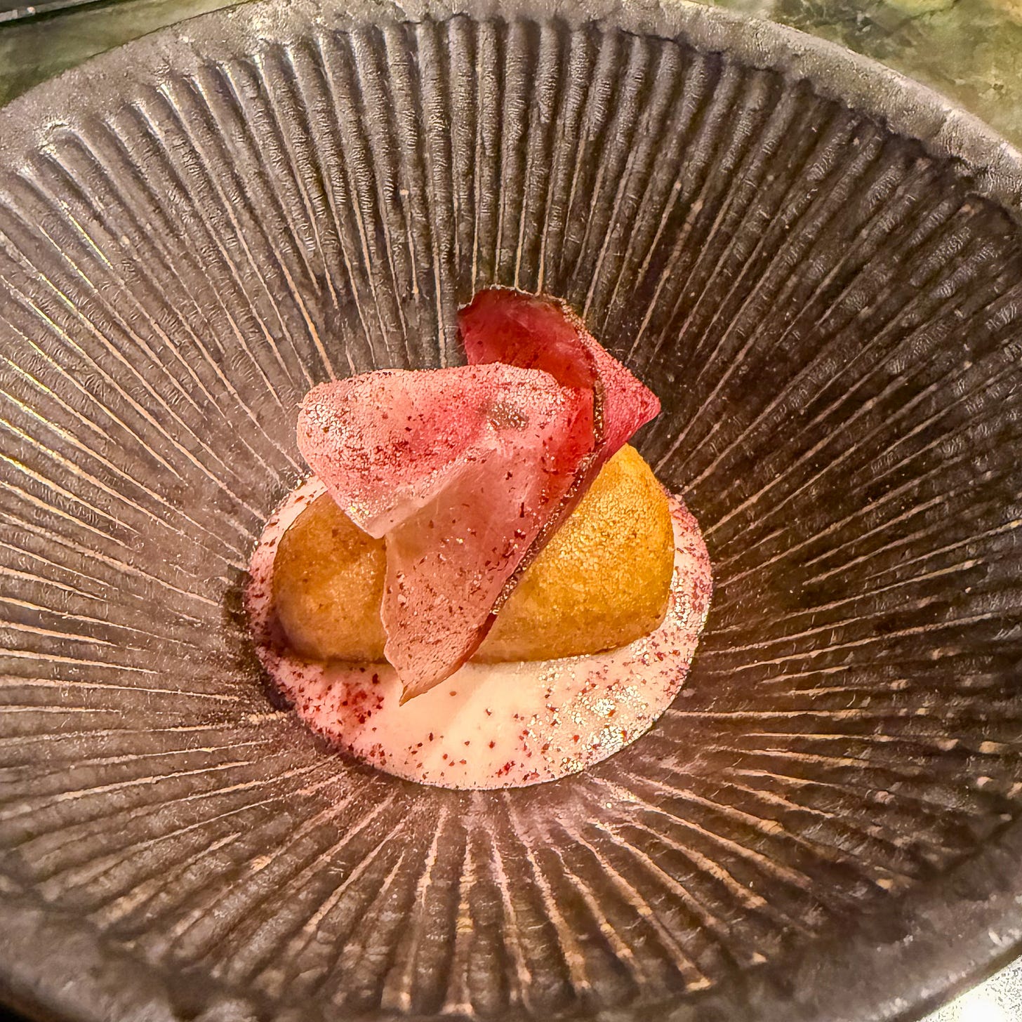 Crispy date beignet with creamy filling on textured glass plate, dusted with pink hibiscus powder at Mantra restaurant