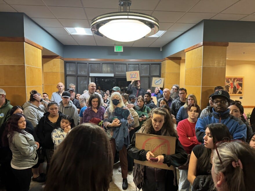 A crowd of protestors with signs gathers inside a hallway.