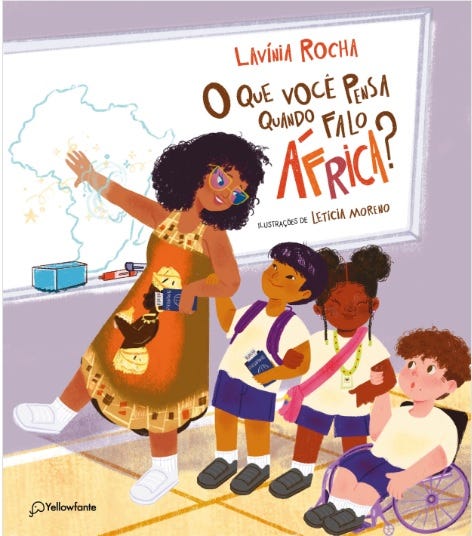 #descrevemospravocê  Capa do livro infantil O que você pensa quando falo África?, escrito por Lavínia Rocha, com ilustrações de Letícia Moreno. A imagem mostra uma cena dentro de uma sala de aula. No centro, uma professora negra de cabelos crespos e soltos, usa vestido marrom com estampas de máscaras africanas e sandálias brancas. Ela sorri e aponta com a mão esquerda para um mapa do Brasil desenhado no quadro branco. Na outra mão, segura cartões pretos com desenhos coloridos.  Ao redor da professora, estão três crianças. À esquerda, uma menina de pele clara, com cabelos pretos e lisos presos em rabo de cavalo, segura um caderno azul. Ao lado, uma menina negra com tranças e mochila vermelha observa atenta, também segurando um caderno. À direita, um menino branco com cabelos castanhos cacheados está sentado em uma cadeira de rodas, sorrindo e segurando um papel. Todos vestem uniformes escolares com camiseta branca e bermuda ou saia azul.  O título do livro aparece em letras grandes e coloridas no canto superior direito, com destaque para a palavra “África”, escrita em vermelho com contorno preto. Abaixo do título, lê-se o nome da ilustradora. No canto inferior esquerdo está o logotipo da editora Yellowfante, com o desenho de um elefante estilizado.  A cena é alegre e educativa, valorizando a diversidade e o ensino sobre a cultura africana no ambiente escolar.