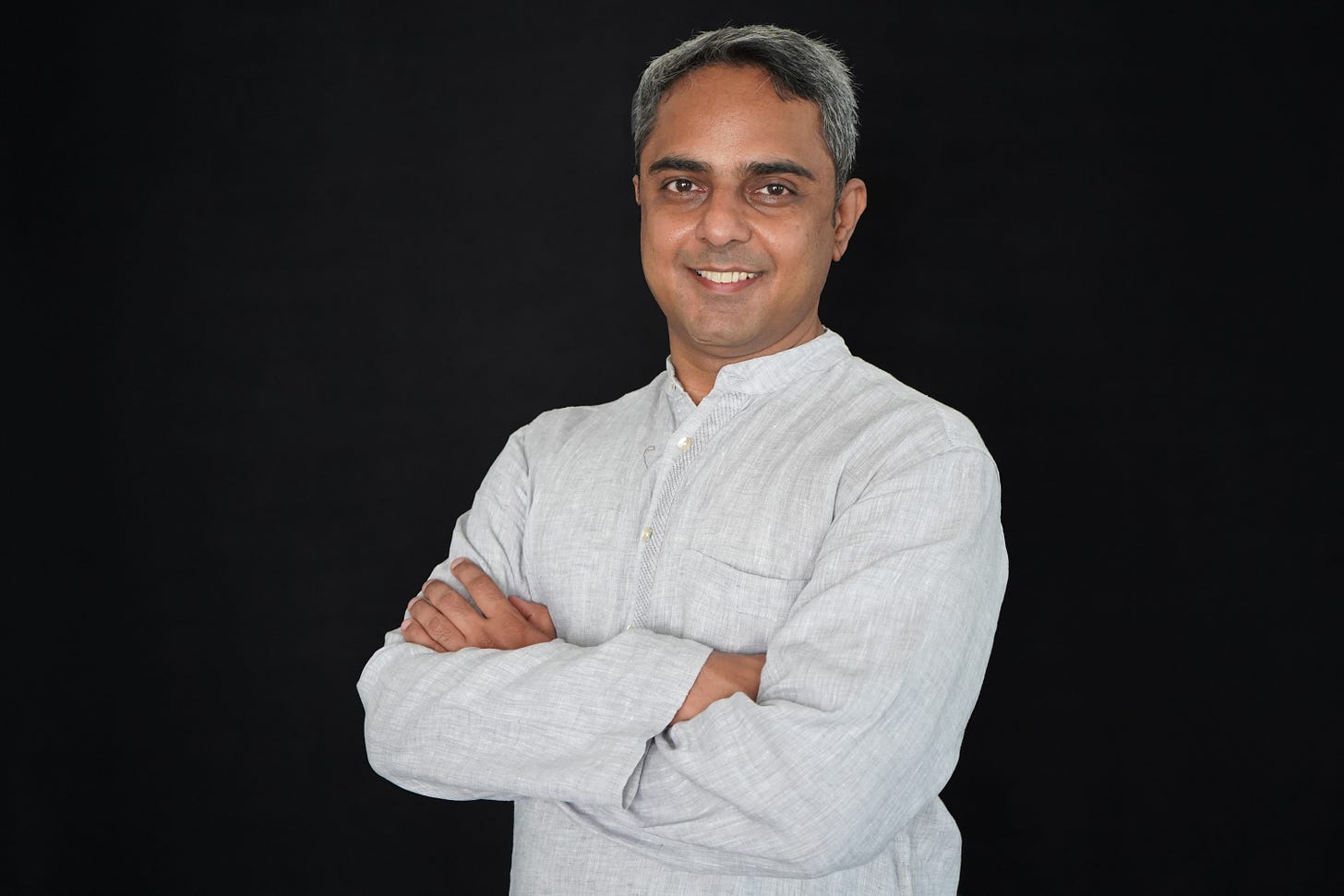 Vishal, an Indian man with short salt and pepper hair is dressed in a grey Mandarin collar full-sleeved kurta and smiling into the camera. Vishal, an Indian man with short salt and pepper hair is dressed in a grey Mandarin collar full-sleeved kurta and smiling into the camera.