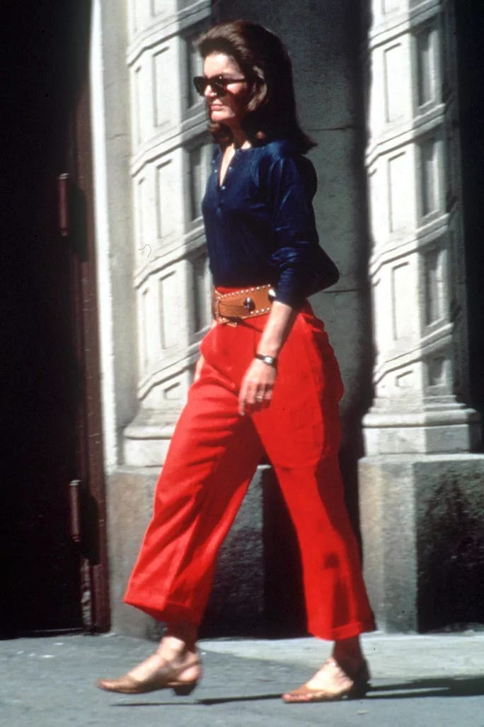 jackie kennedy in red cropped pants with a navy blue dress shirt and camel-colored belt