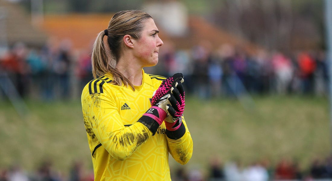 Mary Earps - a female goal keeper wearing gloves and a yellow shirt - standing in front of a crowd looking to the right