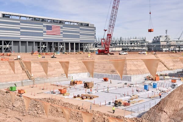 A large construction site, with an excavation several stories below ground and a crane overhead.
