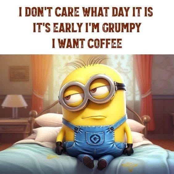 A yellow Minion character with large round goggles sits on a blue bed in a warmly lit bedroom with a lamp nearby. The Minion has a grumpy expression with half-closed eyes and downturned mouth, wearing blue overalls over its body. Text overlay reads I dont care what day it is on top, Its early Im grumpy in the middle, and I want coffee at the bottom.