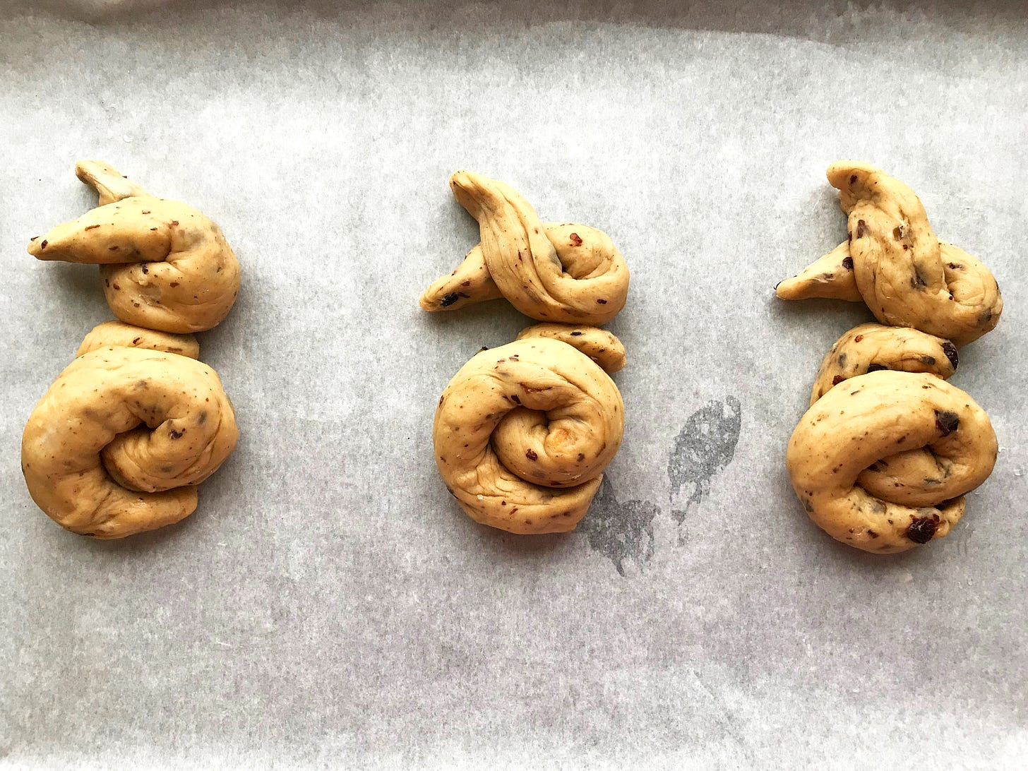 Three hot cross bunnies on a parchment-lined tray ready for proving.