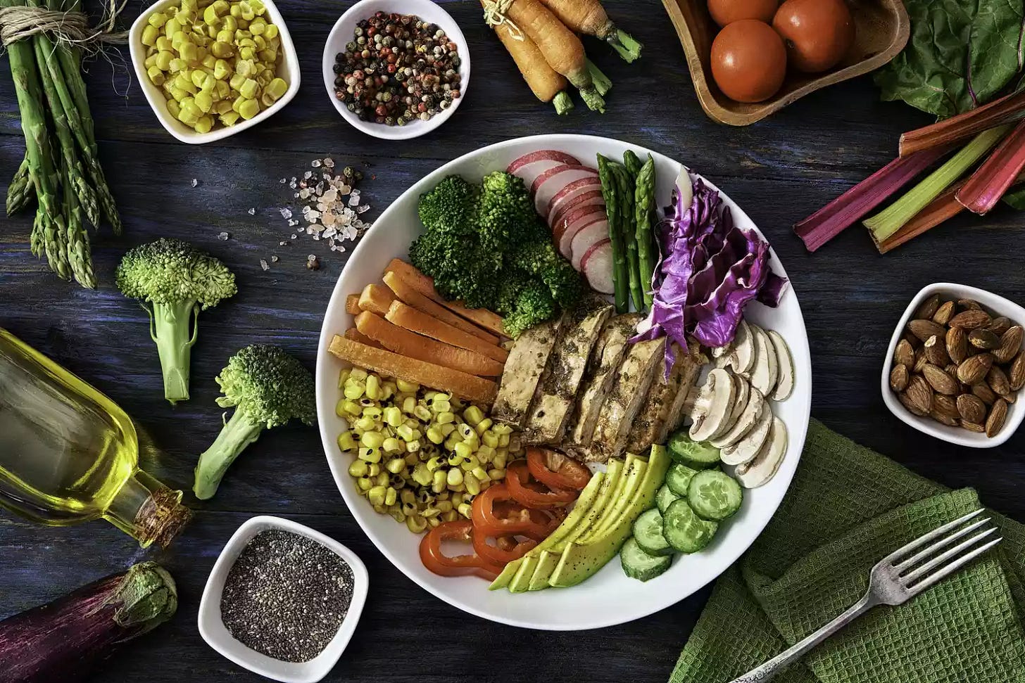 Colorful spring salad on rustic white wood table. Included ingredients: Chicken, tomatoes, broccoli, lettuce, bell peppers, mushroom, carrots, radicchio, almonds.