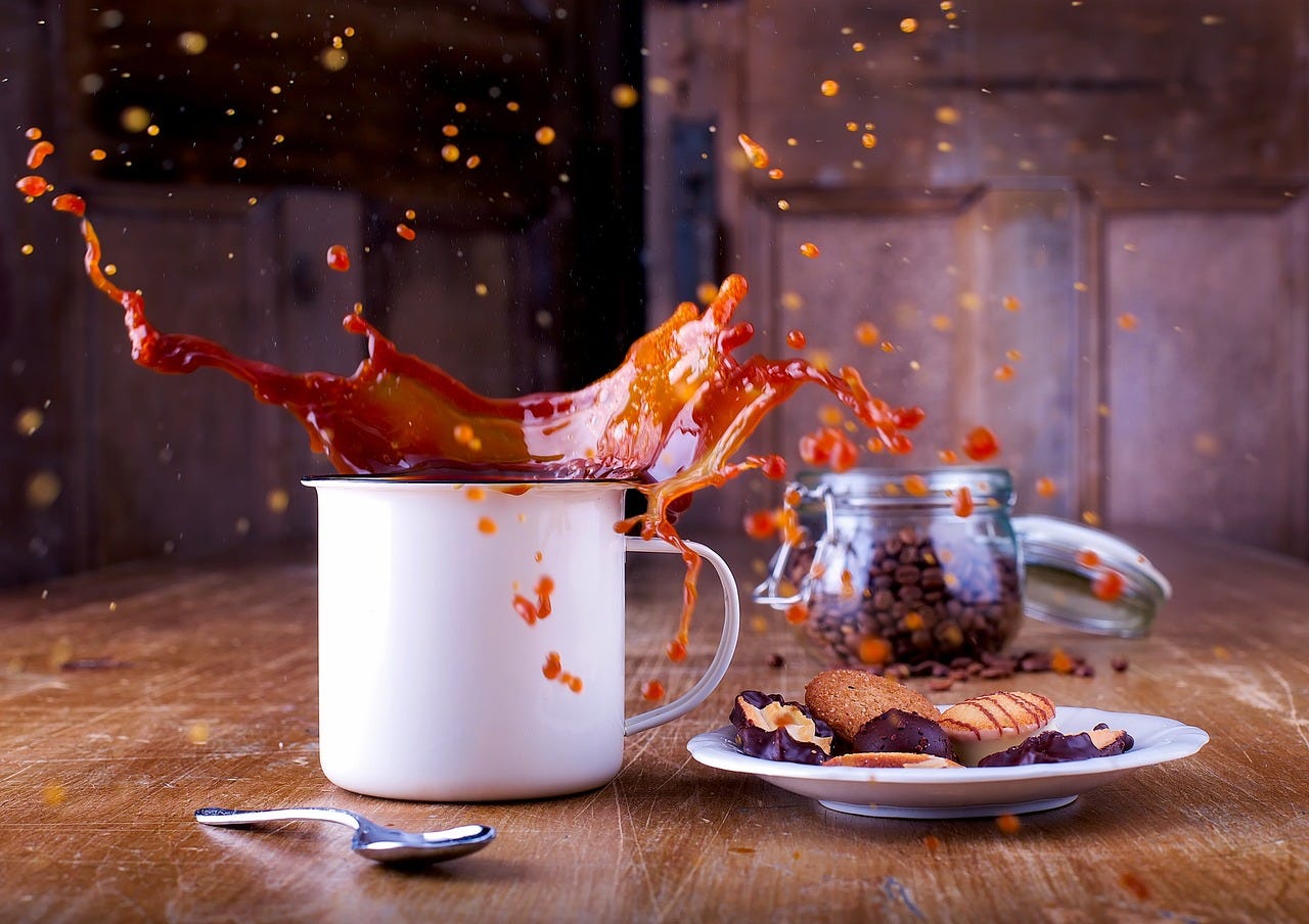 coffee splashing outside mug suggesting a mess on the table spilling over onto the cookies.