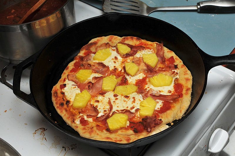 A pizza with pineapple topping in a pan on a stove
