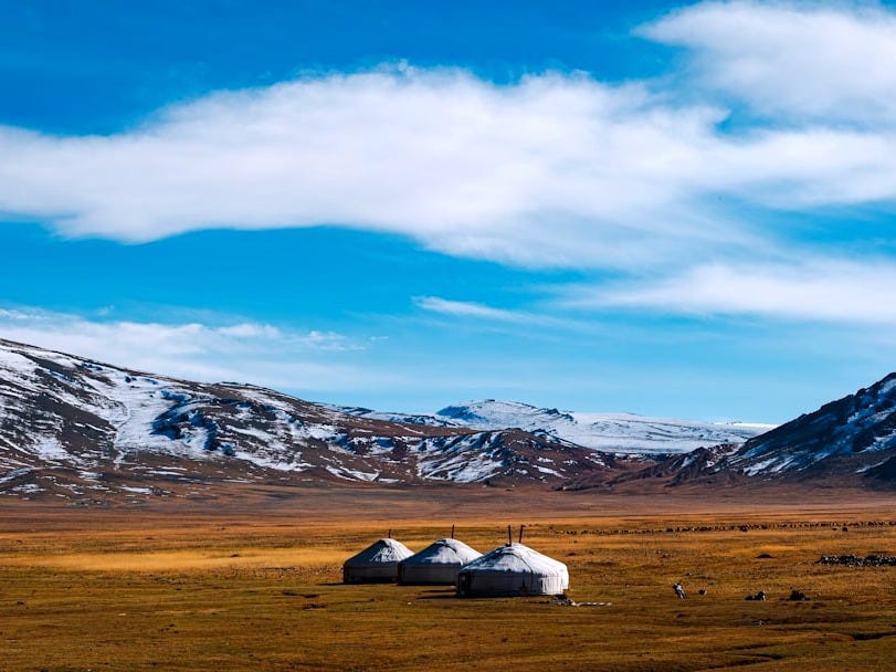 Yurts sit on a steppe before snowy mountains. Yurts sit on a steppe before snowy mountains.