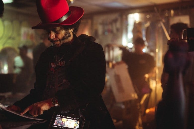 Director Boots Riley wearing a large red hat stares at a piece of paper on a film set. 