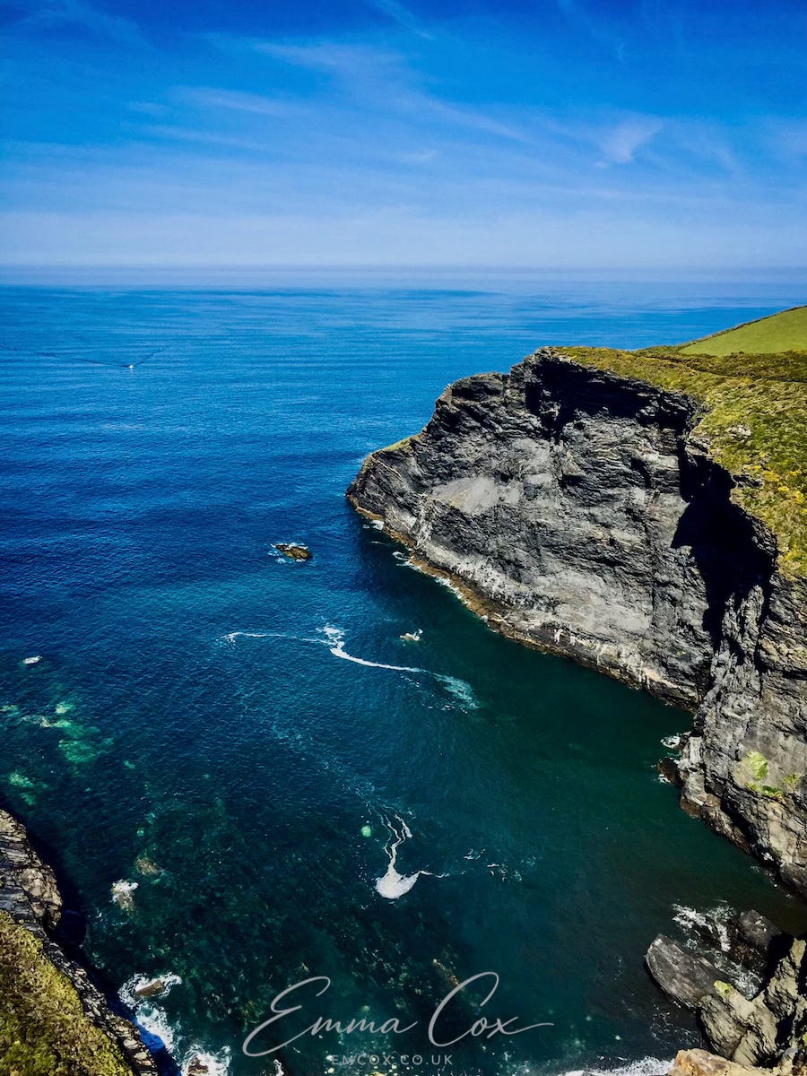 a photo of a cliff face looking out to sea on a calm, sunny day with blue skies