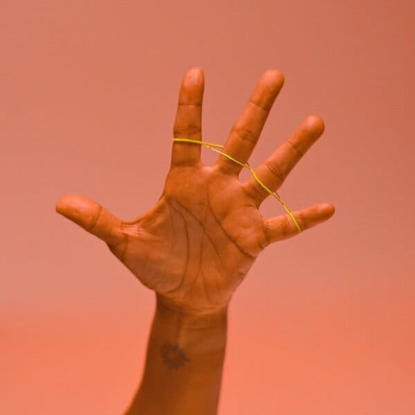 A hand is spread wide with a rubber band threaded between the fingers. A hand is spread wide with a rubber band threaded between the fingers.