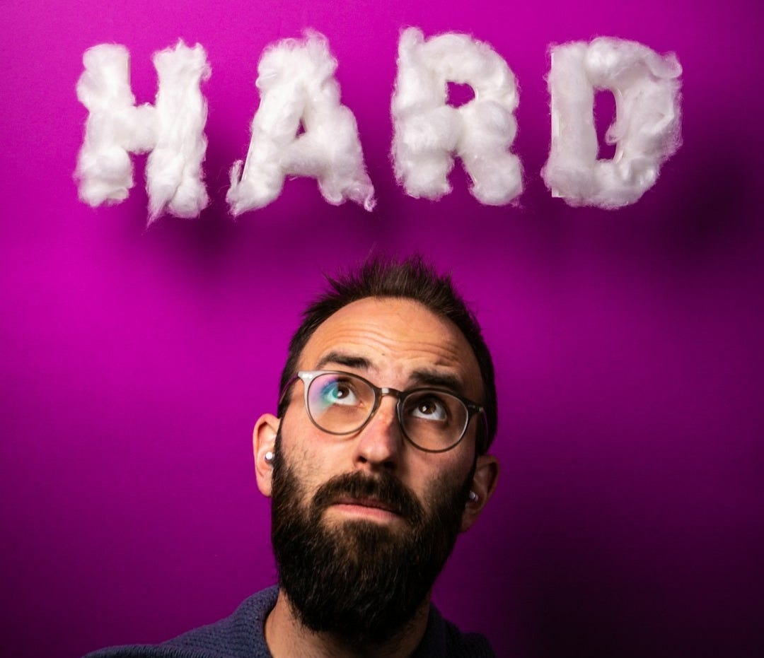 a man with glasses and a beard standing in front of a purple wall with the