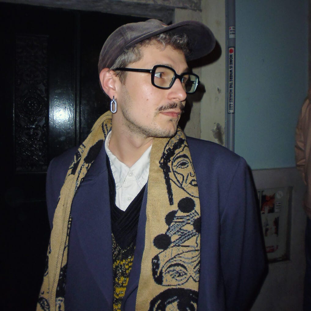 Ray Svitla, wearing glasses, a cap, and a patterned scarf, looking to the side. Ray Svitla, wearing glasses, a cap, and a patterned scarf, looking to the side.