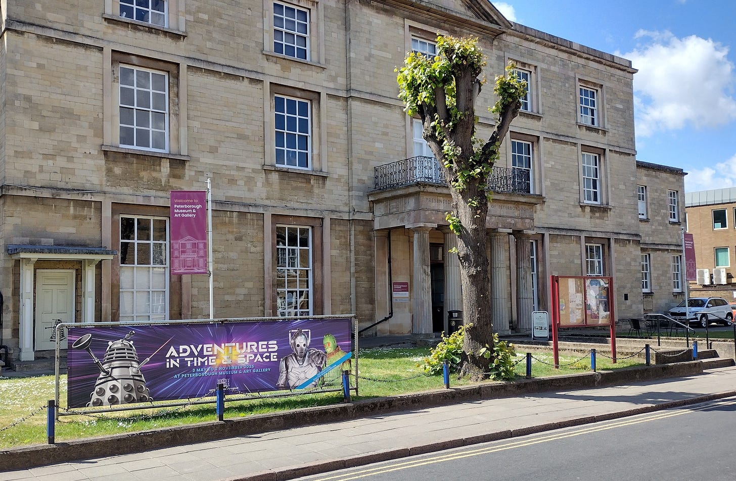 A large building with a small portico with a temporary banner outside advertising the ‘Adventures in Time & Space’ Doctor Who exhibition.