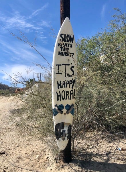 slow down what's the hurry painted on a surfboard mounted to a pole alongside a dirt road in los barriles.