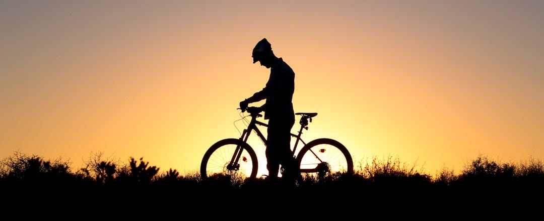 silhouette of man riding bicycle during sunset
