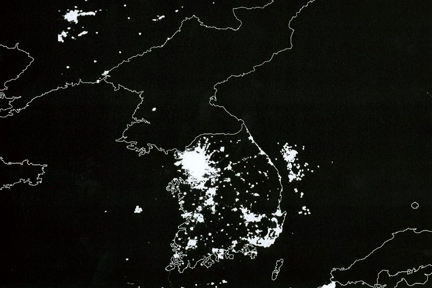 Satellite image of the Korean peninsula at night showing bright city lights in South Korea and almost no lights in North Korea.