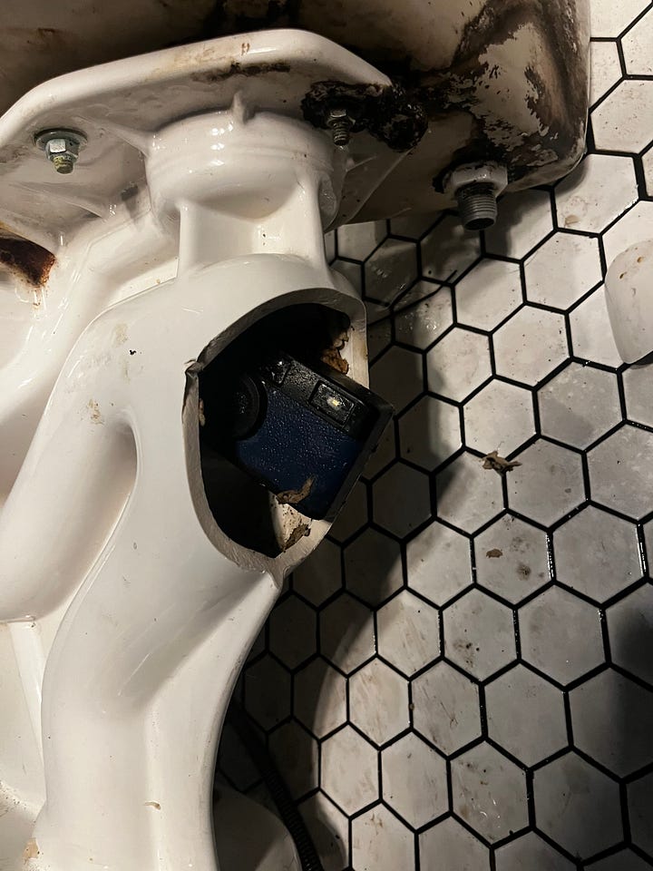 A toilet broken to reveal a plastic camera, the plastic camera being held in front of the toilet