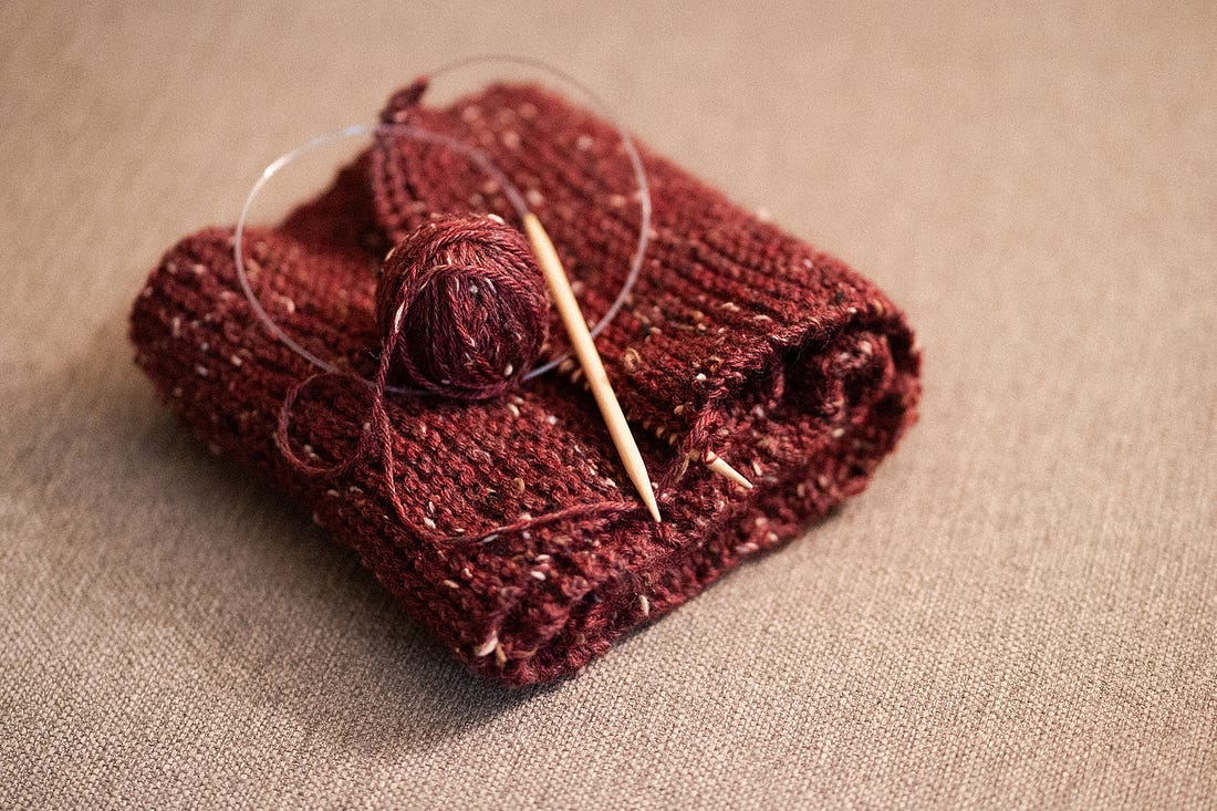 Photo of a red knit scarf with knitting needles and a ball of yarn
