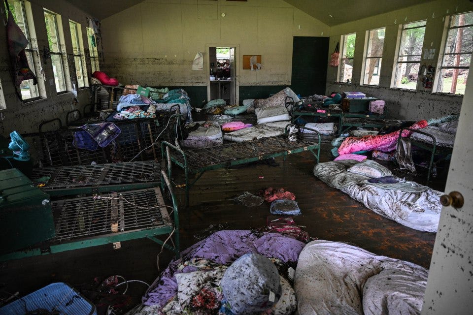 Muddy interior of a flood-damaged cabin with overturned beds and belongings.
