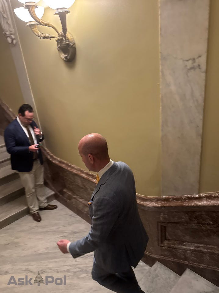 A bald man descenda a stairwell in a suit as another checks his phone in background A bald man descenda a stairwell in a suit as another checks his phone in background