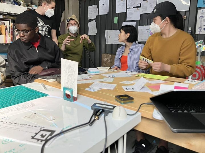 people around a table looking at programs all spread out & lit up by the projector above head