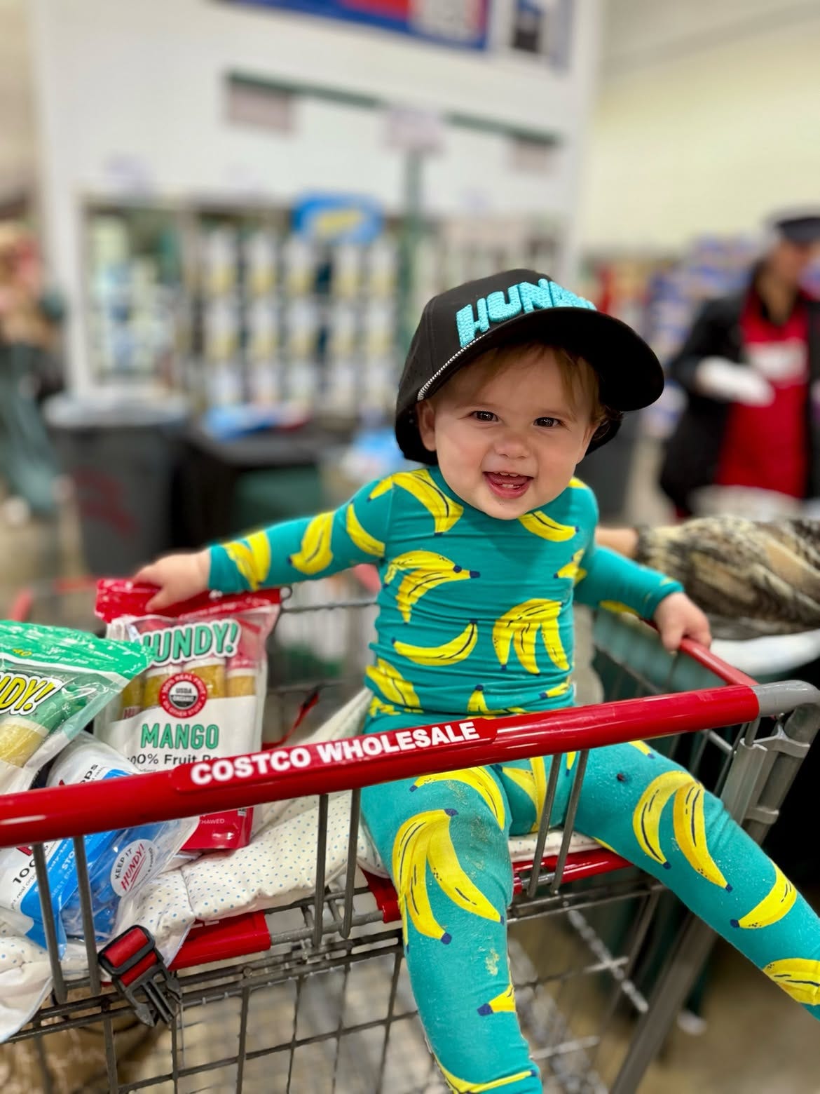 Zoe in a teal and yellow banana onesie sitting in a costco shopping cart Zoe in a teal and yellow banana onesie sitting in a costco shopping cart