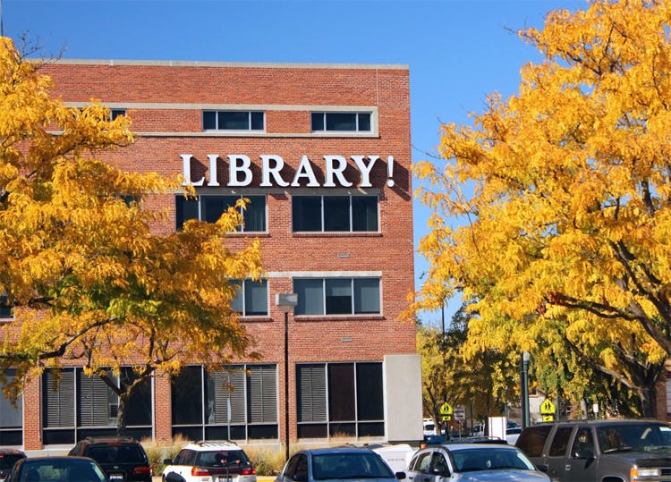 Color photo on clear fall day of Boise's main library, a 3-story red brick building with a sign reading 'Library!' — complete with exclamation point, which was donated in the 1990s by a local pizzeria owner who thought people should be excited about their library.