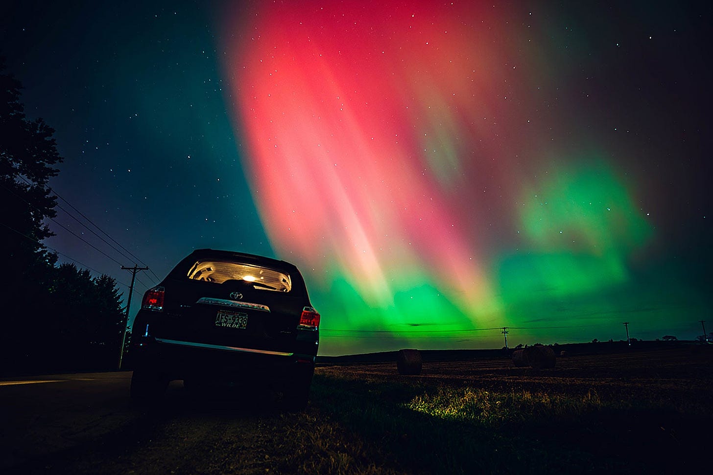 Aurora borealis glowing in vibrant green and pink hues over a rural landscape at night Aurora borealis glowing in vibrant green and pink hues over a rural landscape at night