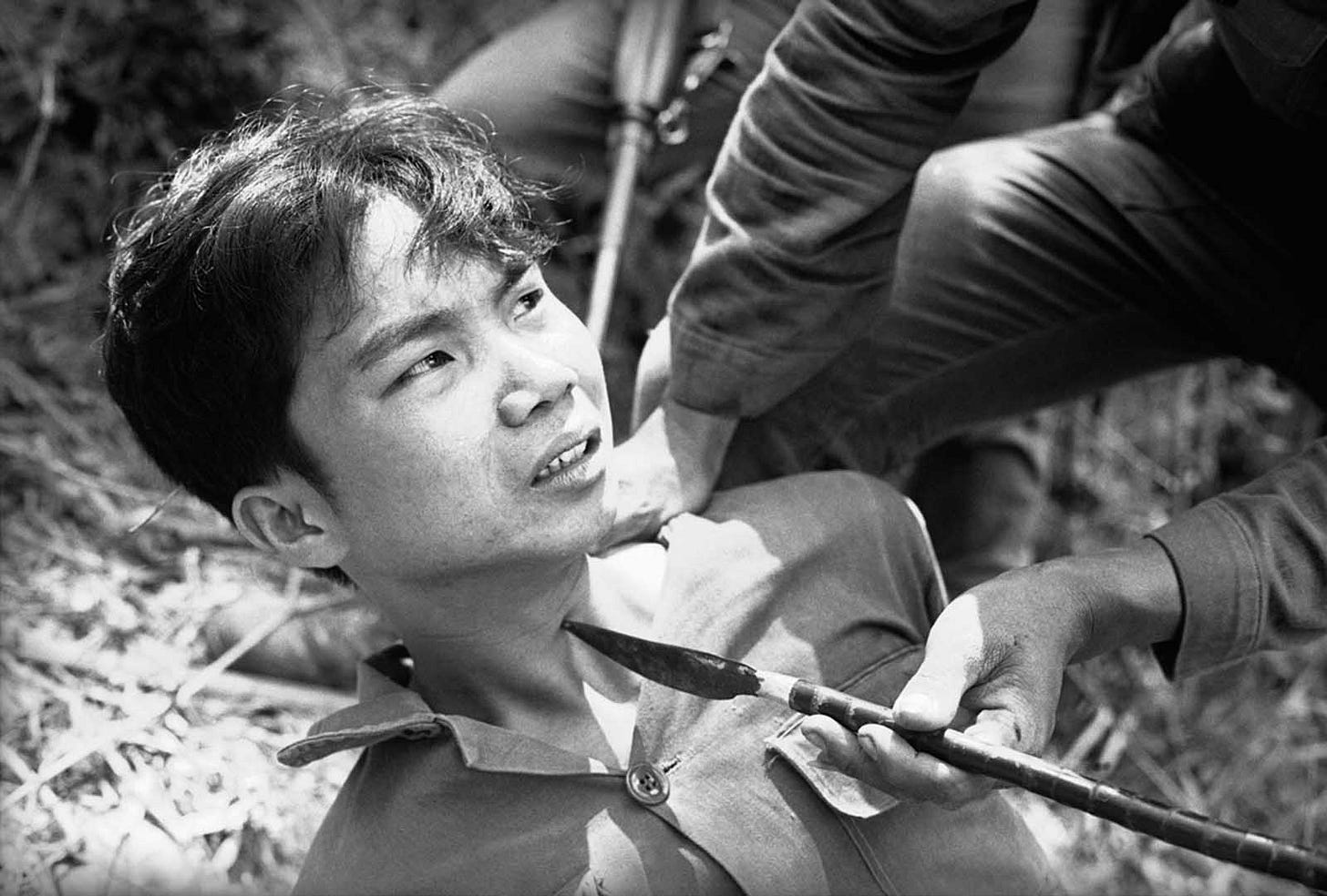 A captured Viet Cong guerrilla, under duress, reveals the location of a Chinese grenade cache to interrogators near Da Nang on March 28, 1965, following the capture of his unit by Vietnamese battalions. A captured Viet Cong guerrilla, under duress, reveals the location of a Chinese grenade cache to interrogators near Da Nang on March 28, 1965, following the capture of his unit by Vietnamese battalions.