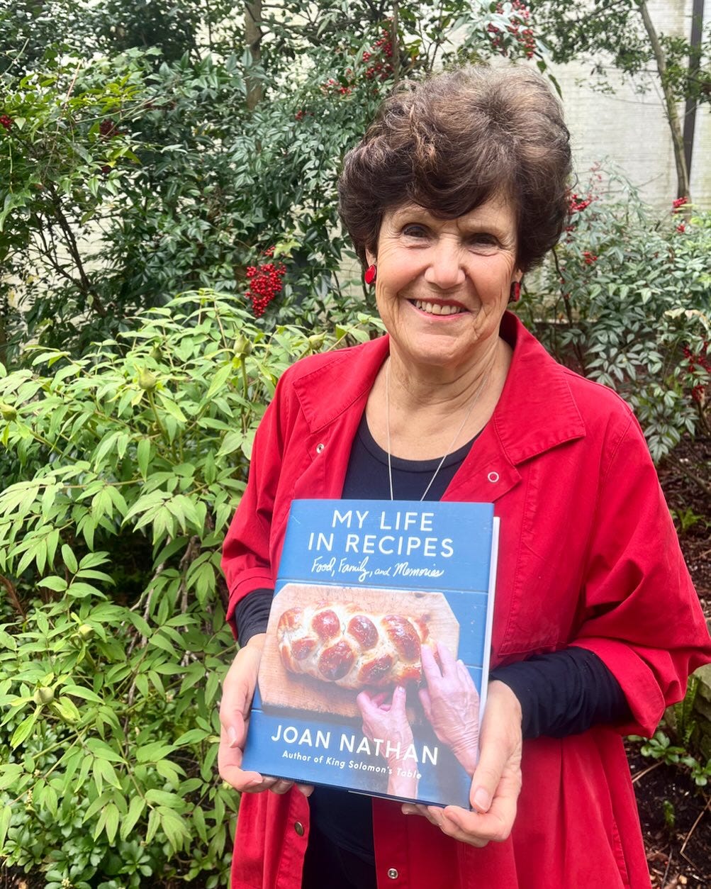 Joan Nathan in a red coat standing outside and holding her book My Life in Recipes Joan Nathan in a red coat standing outside and holding her book My Life in Recipes
