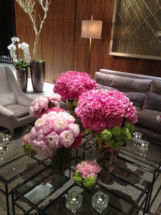 This may contain: a living room filled with lots of furniture and flowers on top of a glass table
