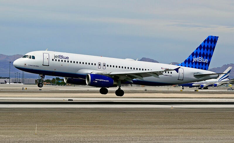 A passenger jet in JetBlue livery with its landing gear extended about to land on a runway. A passenger jet in JetBlue livery with its landing gear extended about to land on a runway.