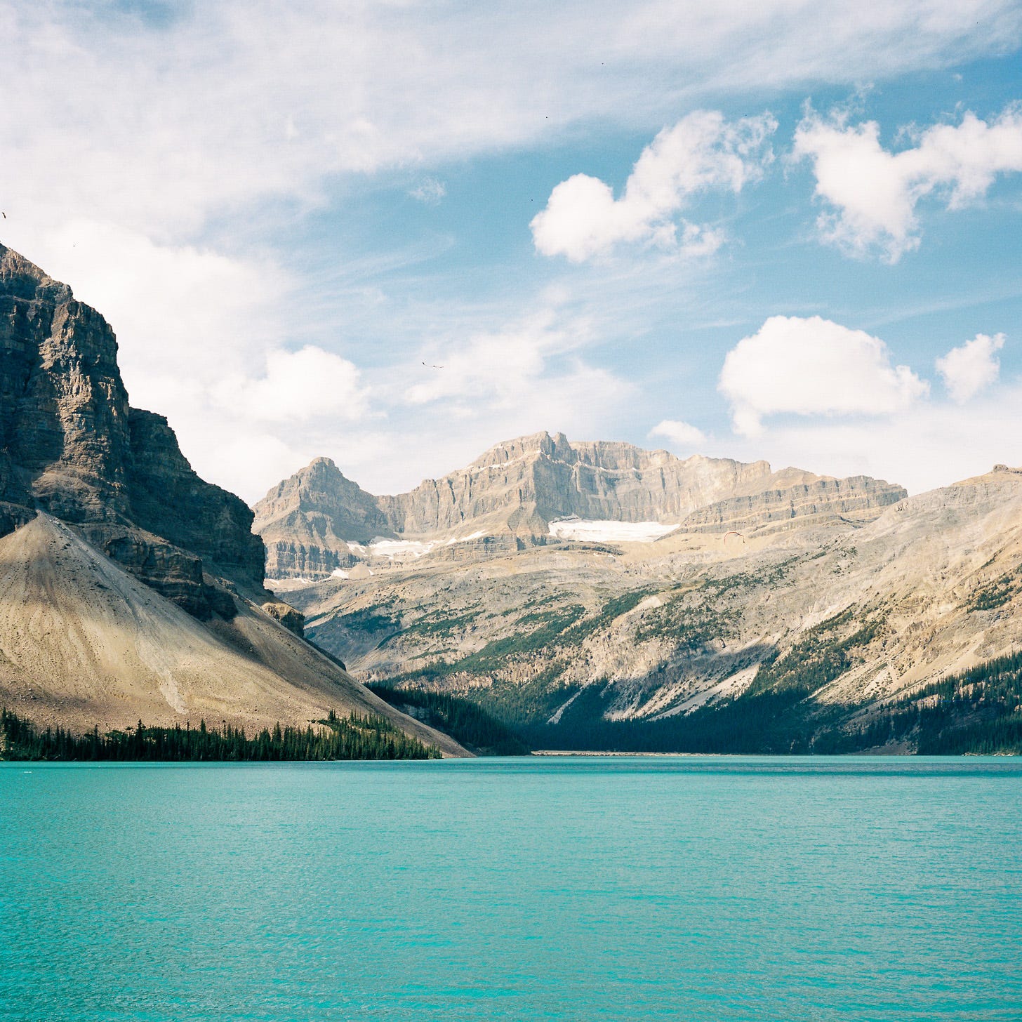 Photo of mountains towering over a light blue lake Photo of mountains towering over a light blue lake