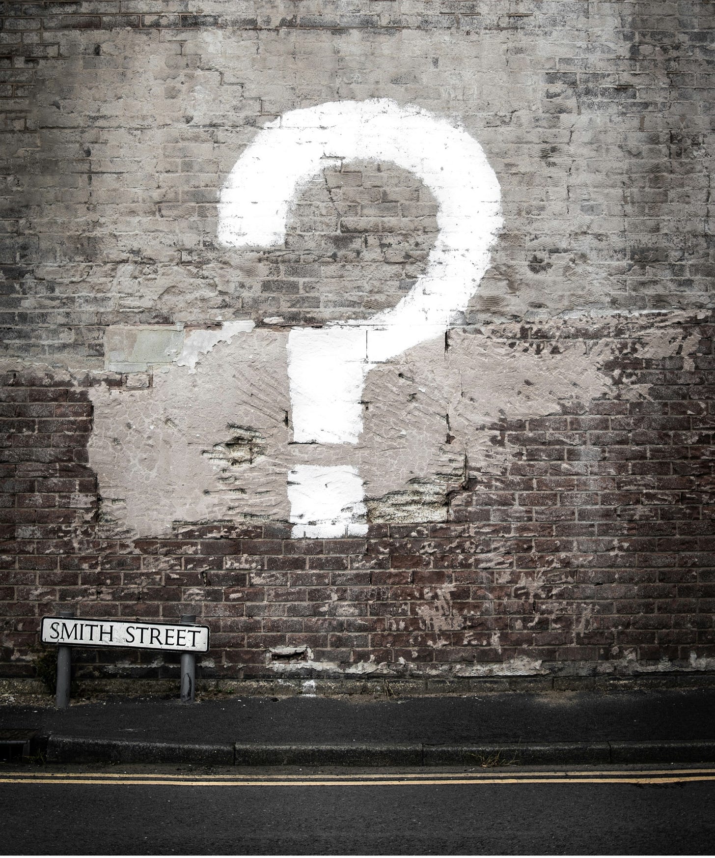 A white question mark painted on a grey brick wall. 