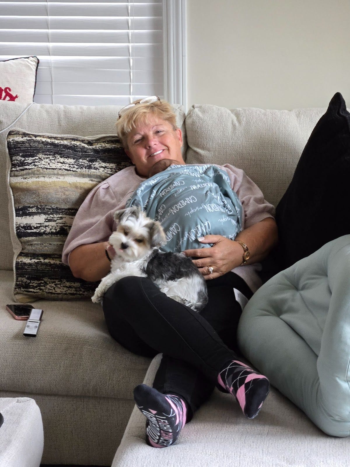 Woman on couch holding a baby, with dog on her lap