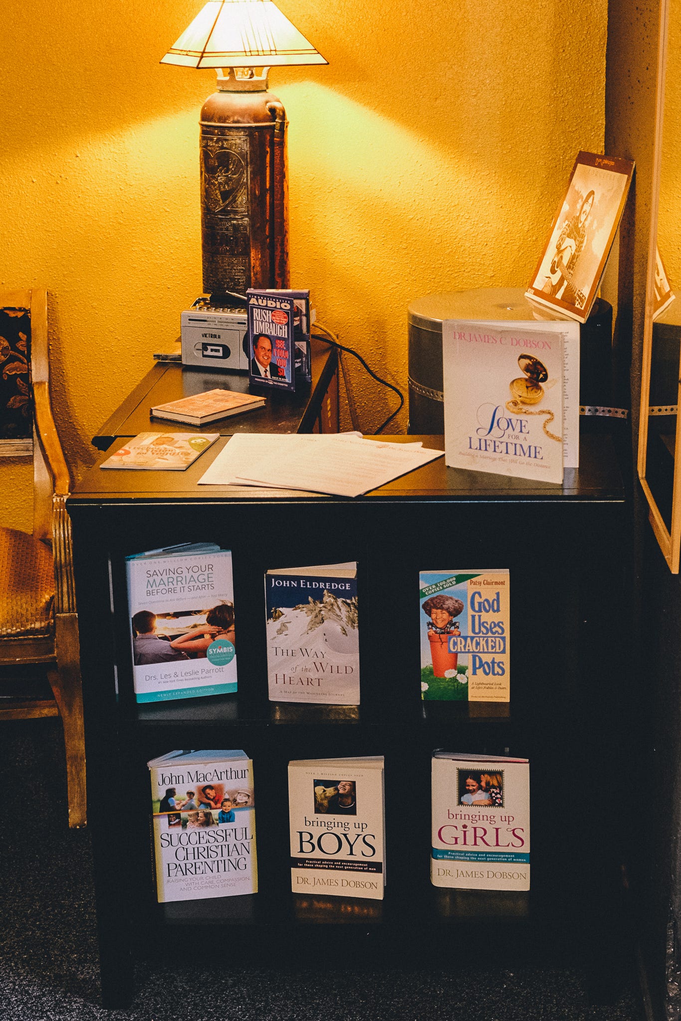 another bookshelf against a yellow wall with a rush limbaugh audiobook and various focus on the fmaily materials on patriarchal marriages