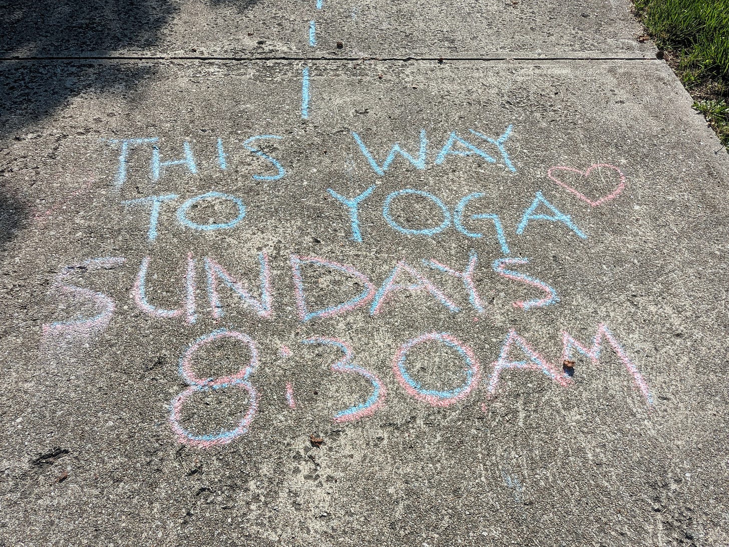 Chalk writing in a concrete driveway "This way to yoga Sundays 8:30AM"