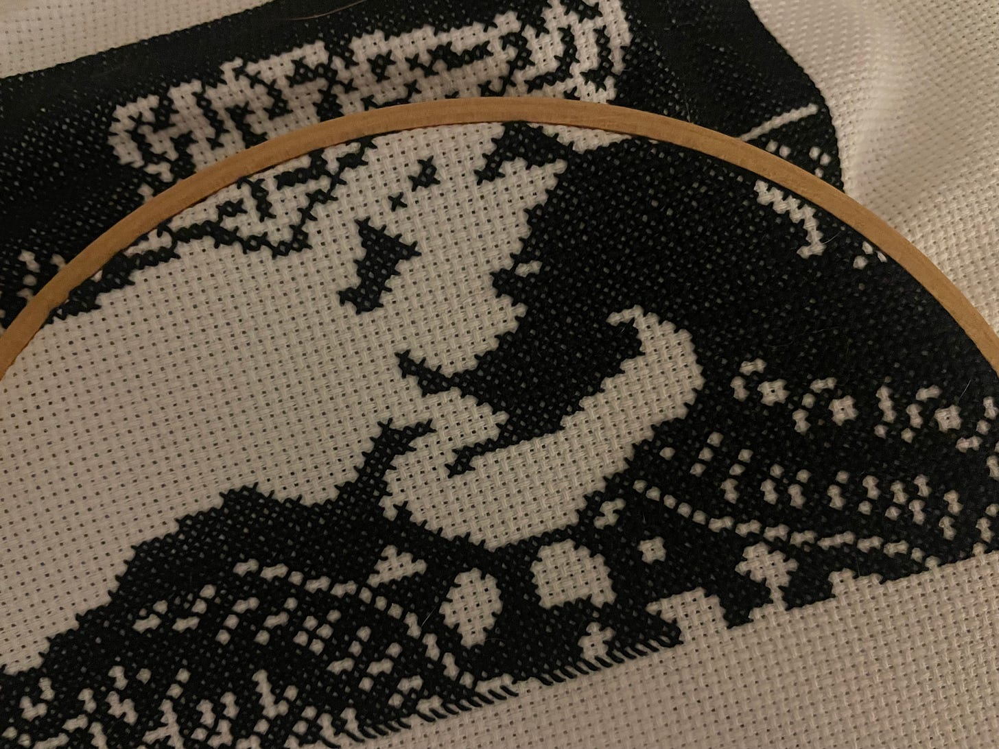 A close up of a black and white cross-stitch project depicting a lounging nude surrounded by printed linens.