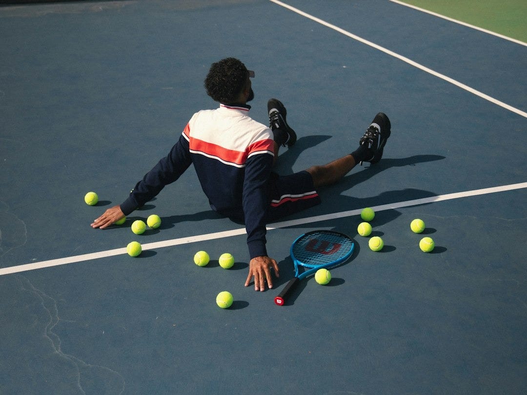 A man laying on a tennis court surrounded by tennis balls A man laying on a tennis court surrounded by tennis balls