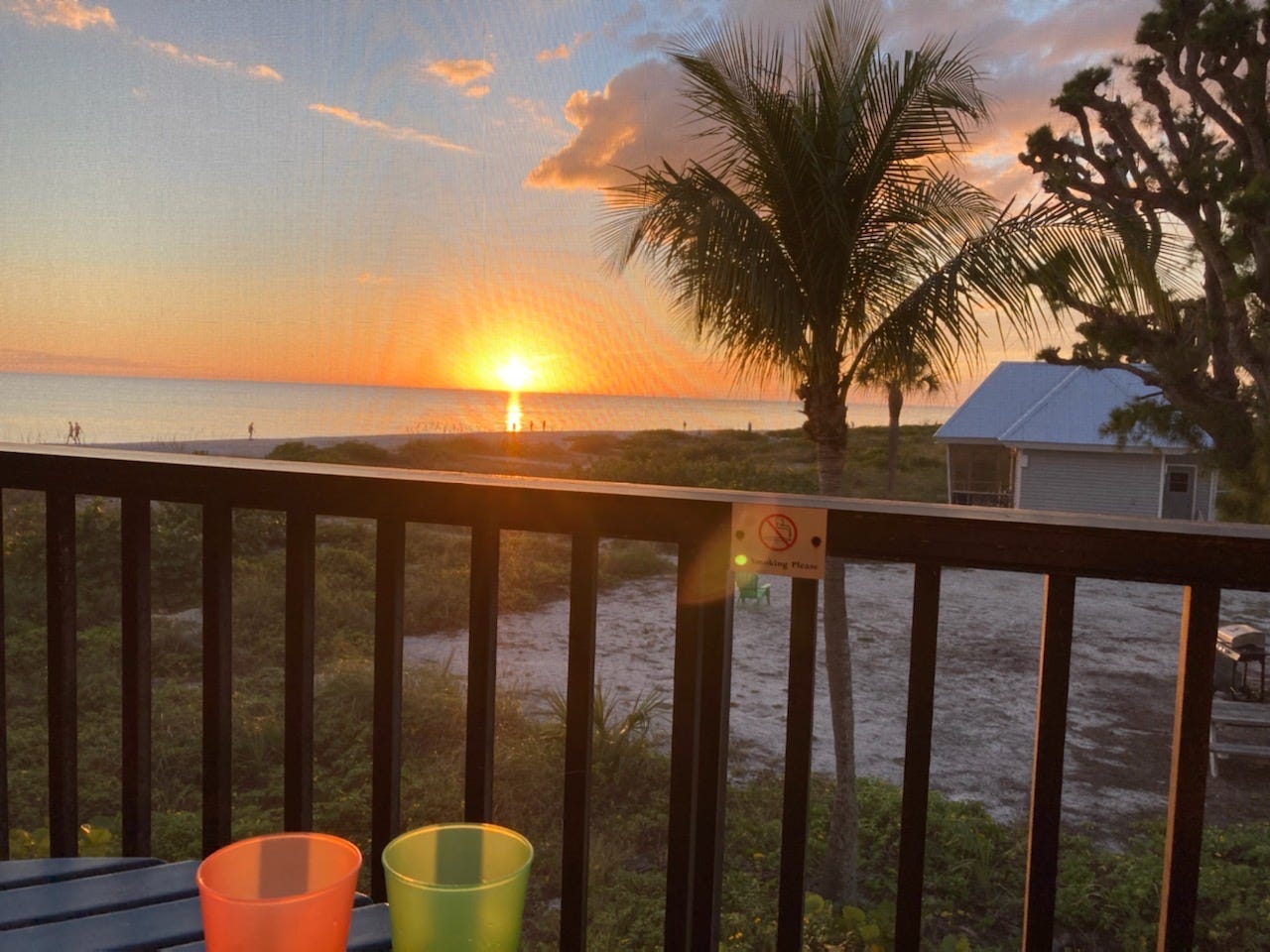 Sunset over the beach with palm trees and a little cottage in the foreground