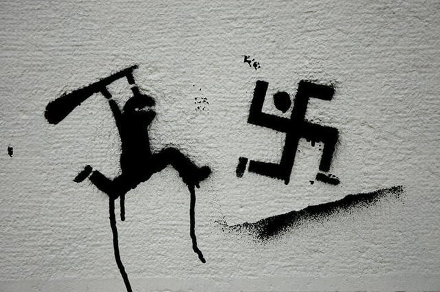 Stencil graffiti of a ninja like figure attacking an antropomorphised swatsika