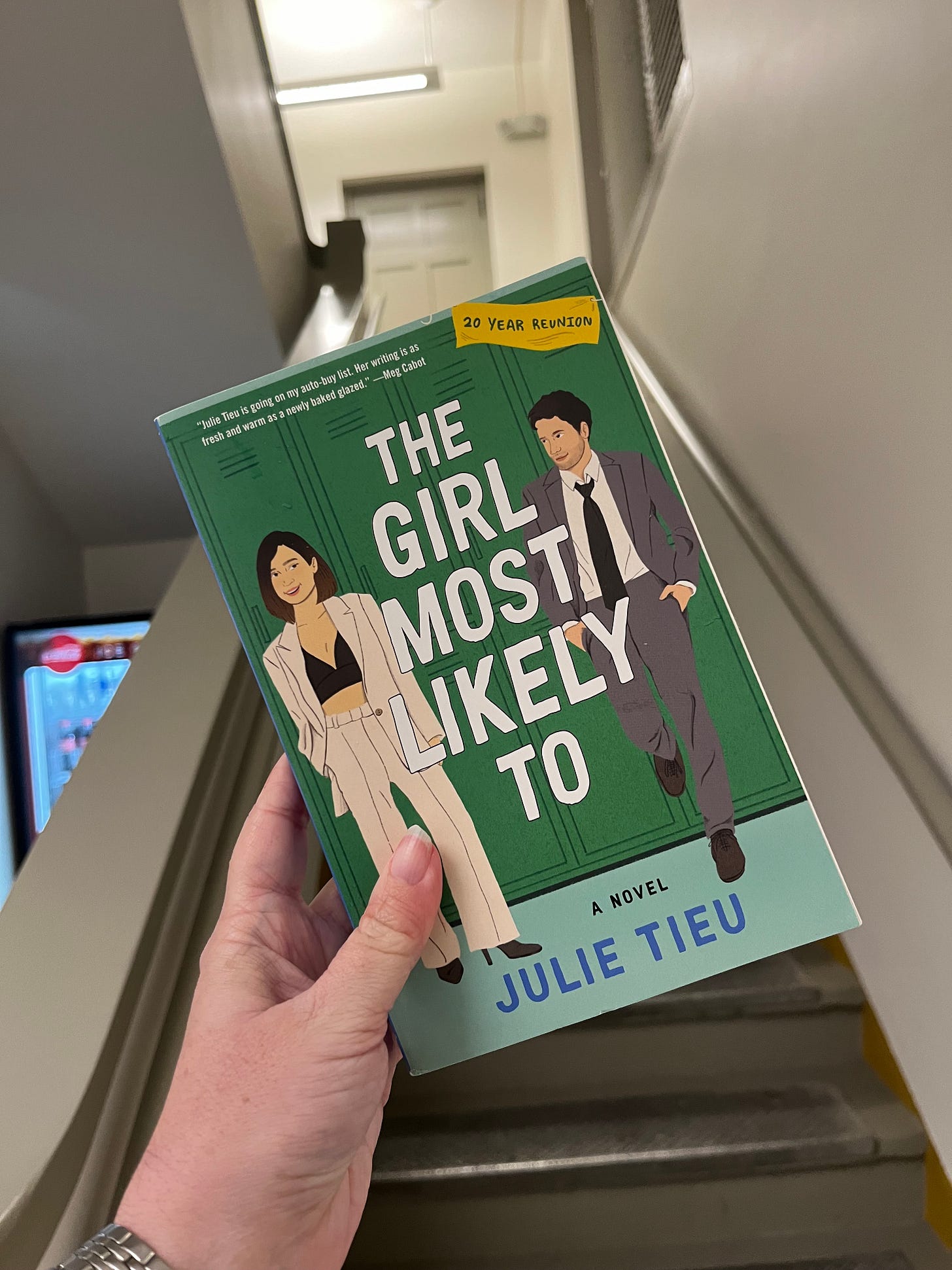 Photo of my hand holding up a copy of THE GIRL MOST LIKELY TO by Julie Tieu in front of a staircase Photo of my hand holding up a copy of THE GIRL MOST LIKELY TO by Julie Tieu in front of a staircase