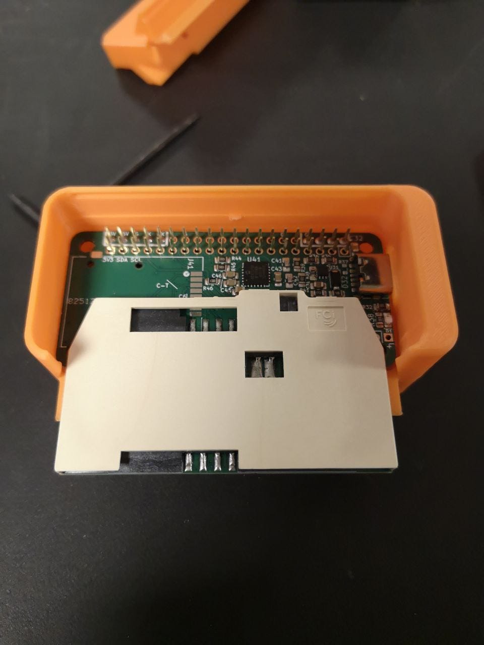 An open orange 3D-printed enclosure showing the custom smartcard reader board stacked on a Raspberry Pi Zero. An open orange 3D-printed enclosure showing the custom smartcard reader board stacked on a Raspberry Pi Zero.