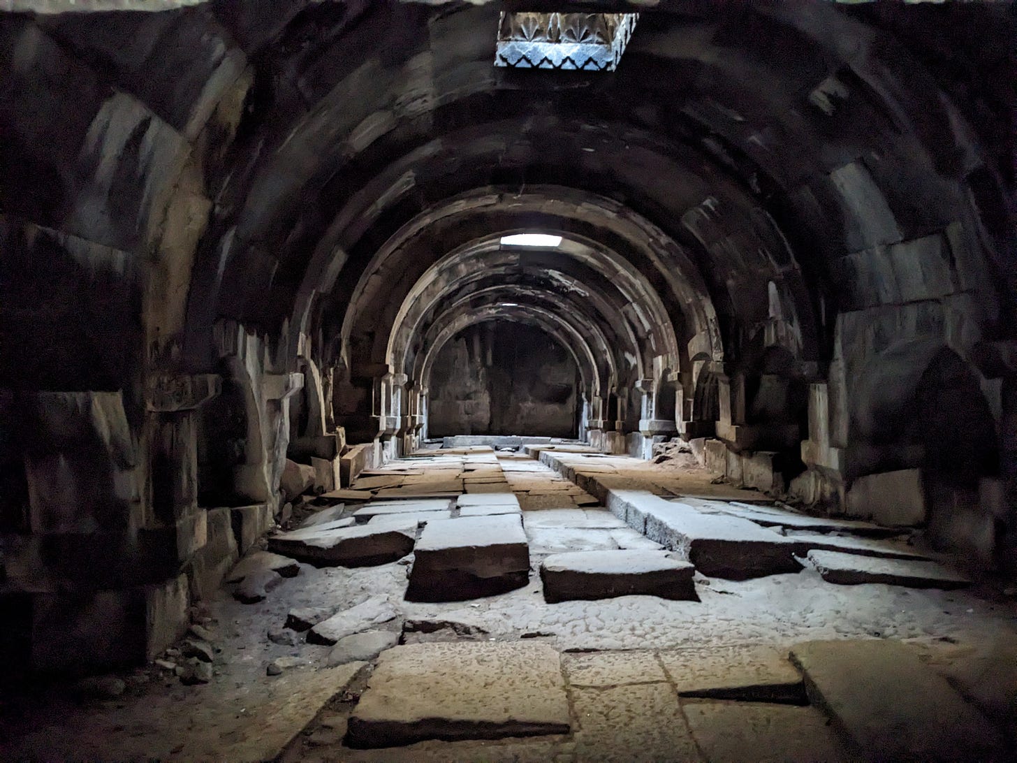 The inside of this ancient stone caravanserai is grey and dark, with shadows from the light coming in from the roof.  