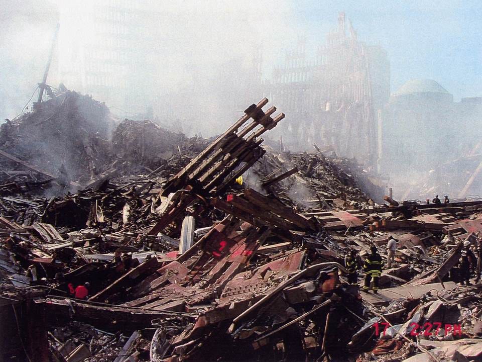 Smoking pile of twisted steel and rubble at Ground Zero with firefighters climbing across the debris