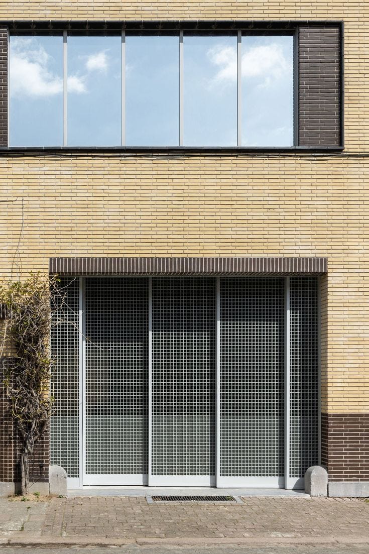 This may contain: an empty street in front of a brick building with windows on each side and plants growing out of the window