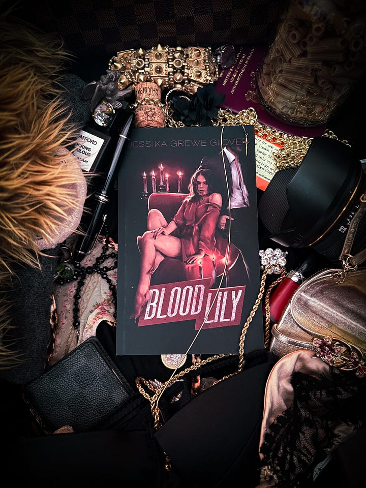 Left: smiling dark haired woman in black top, holding the book, BloodLily. Right: flat lay consisting of the book BloodLily, surrounded by various items including a train ticket from London to Exeter, a highland cow plushie, and jewelry
