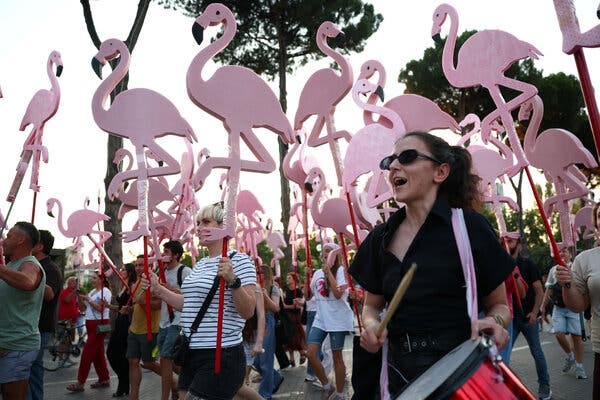 Many protesters march outside and hold pink flamingo figurines.